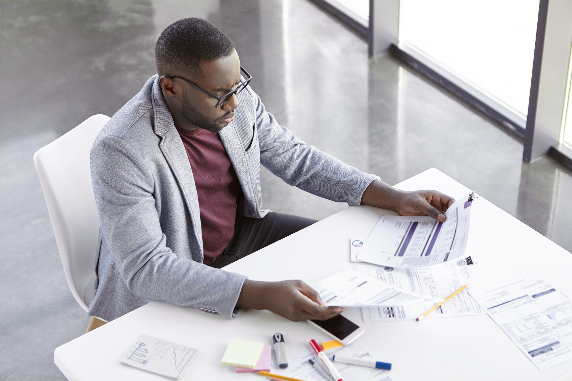 Business owner reviewing financial paperwork at a desk by large office windows.